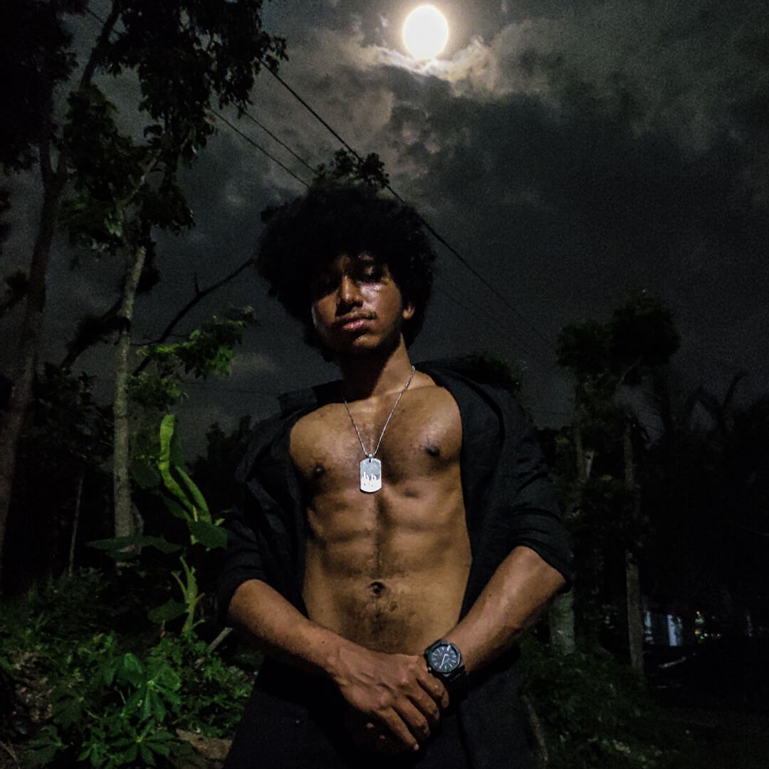 a shirtless bodybuildr in a black shirt wearing a dog tag standing in front of a full moon with a wrist watch on his hand