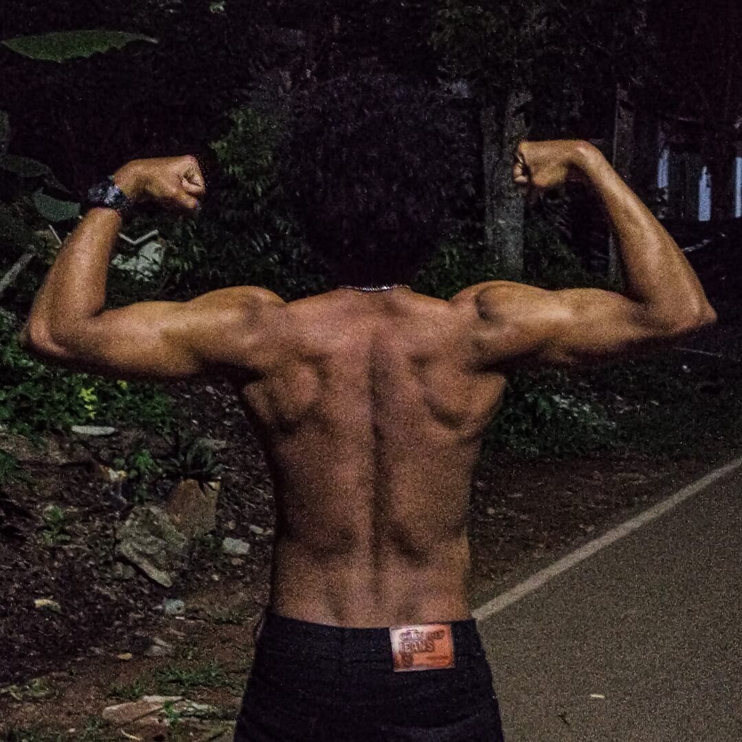 the back of a bodybuilder flexing his muscles at night on a road
